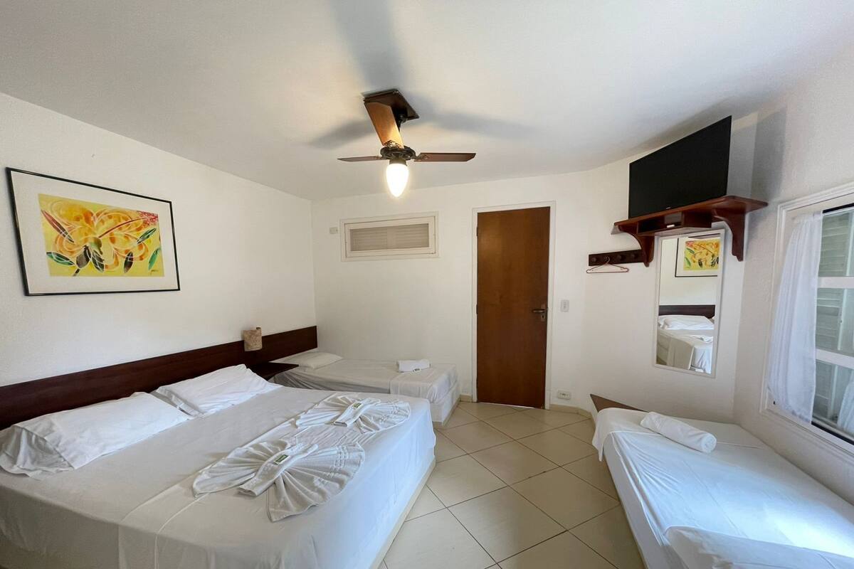 Une chambre d’hôtel avec deux lits, un ventilateur de plafond, une fenêtre avec des rideaux et un téléviseur fixé au mur.