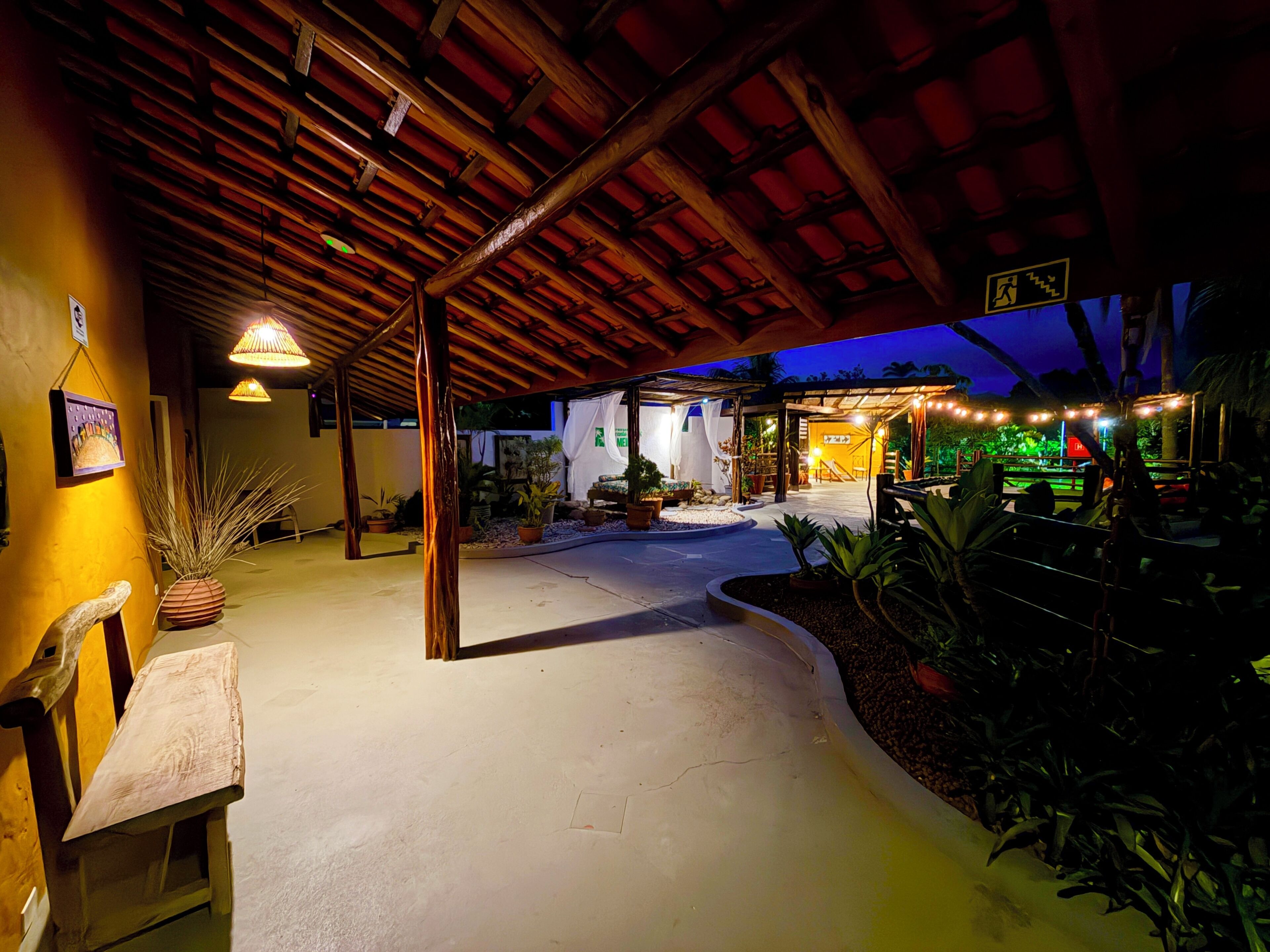 An outdoor covered area with a wooden ceiling, potted plants, and a pathway leading to a building.