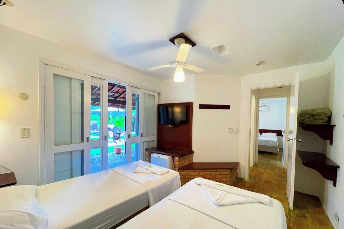 Une chambre d’hôtel avec deux lits simples, un ventilateur de plafond, une télévision et une vue sur l’extérieur.