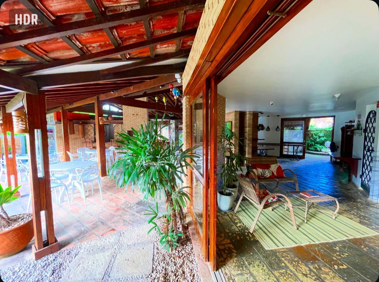 A spacious indoor area with a wooden ceiling, potted plants, and a seating area with chairs and a table.