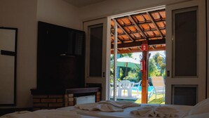 Ein Hotelzimmer mit Bett, Fernseher, Kamin und Blick auf den Außenbereich mit Pool und Stühlen.