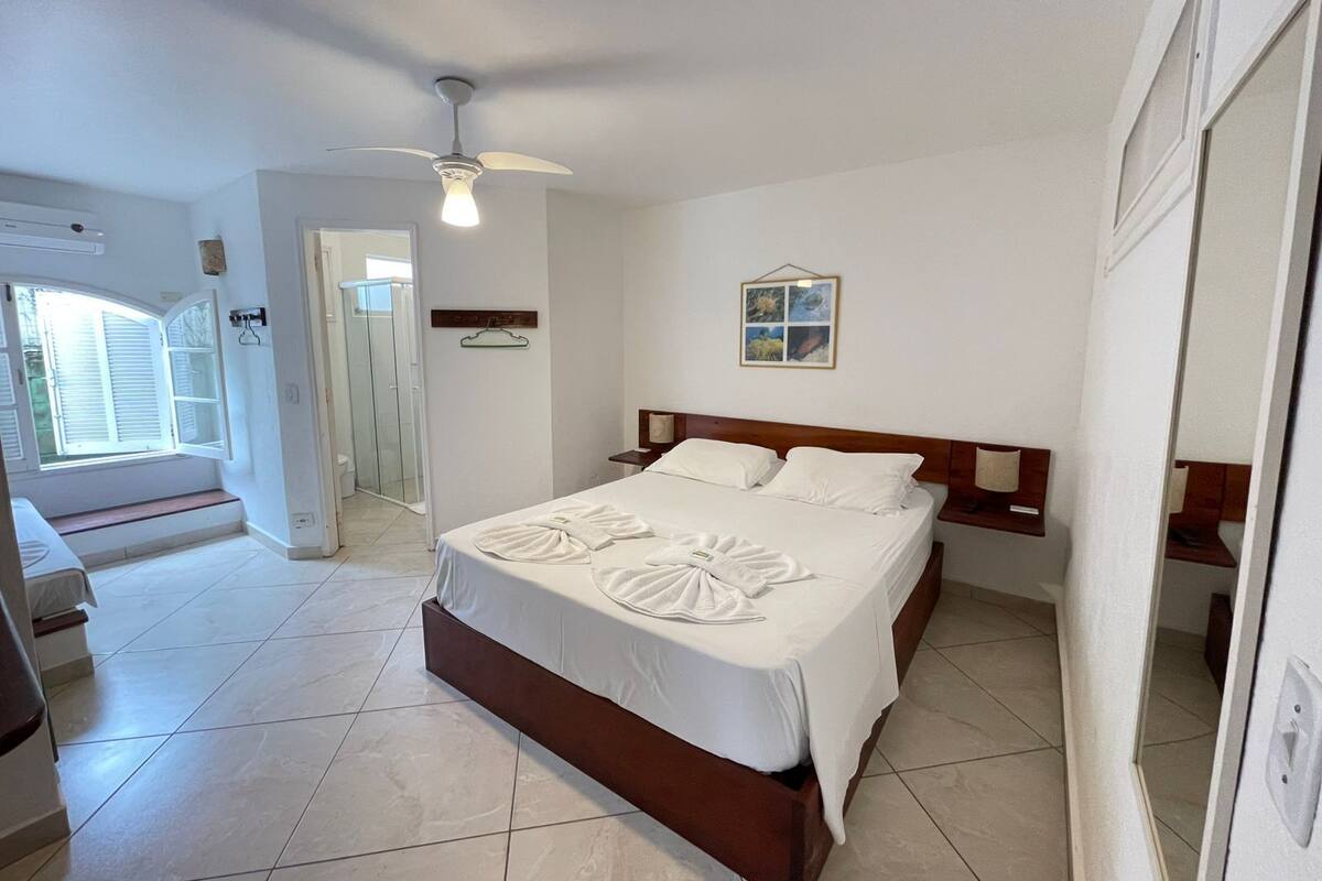 Une chambre d’hôtel avec un lit, un ventilateur de plafond, une douche et un petit tableau accroché au mur.