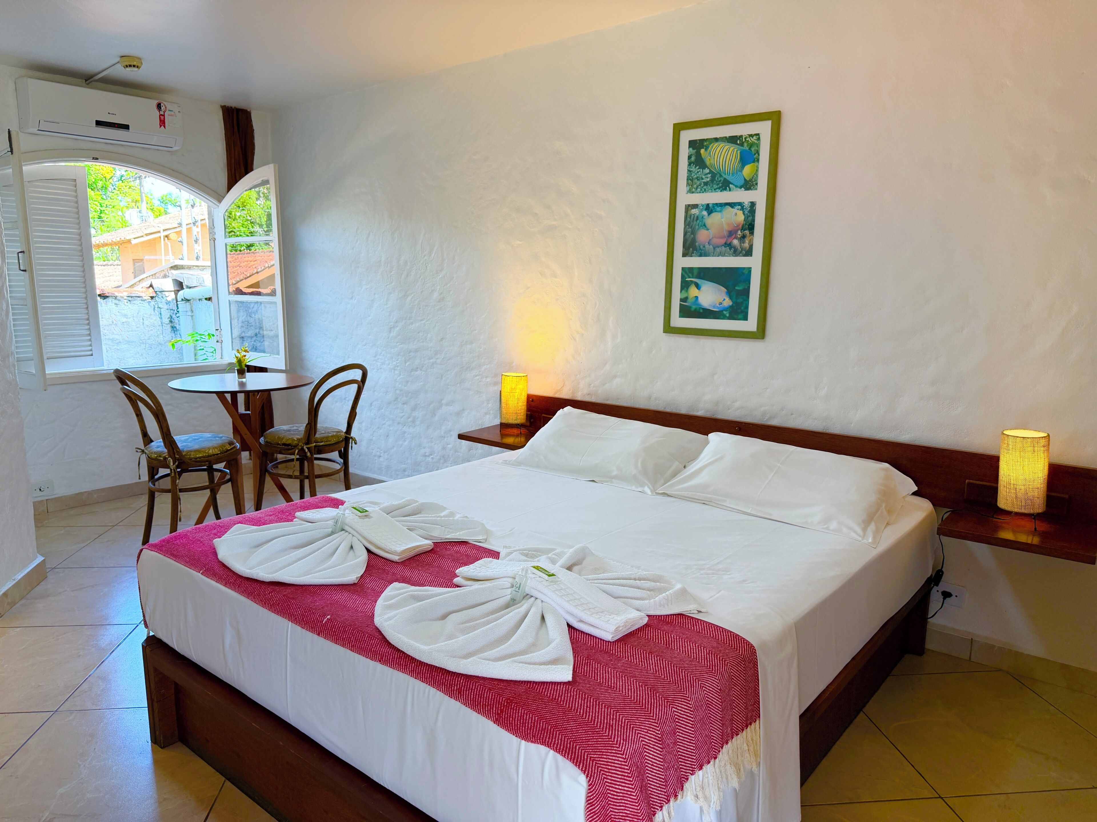 Una camera d'albergo con un letto, un tavolo da pranzo con sedie, un tavolino con una lampada e una parete decorata con quadri.