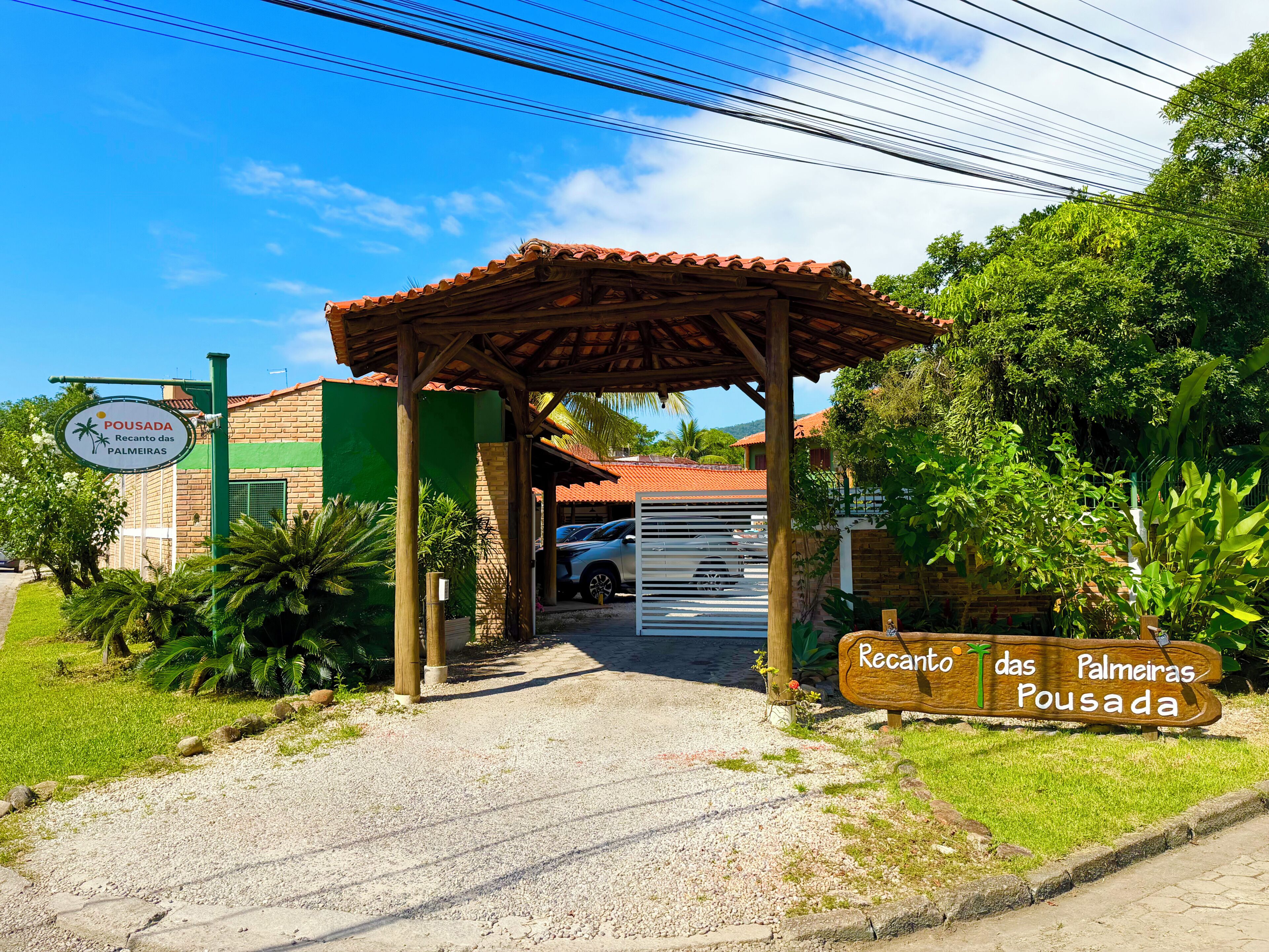 A building entrance with a covered walkway, a sign indicating 'Recanto das Palmeiras Pousada,' and a parked car.