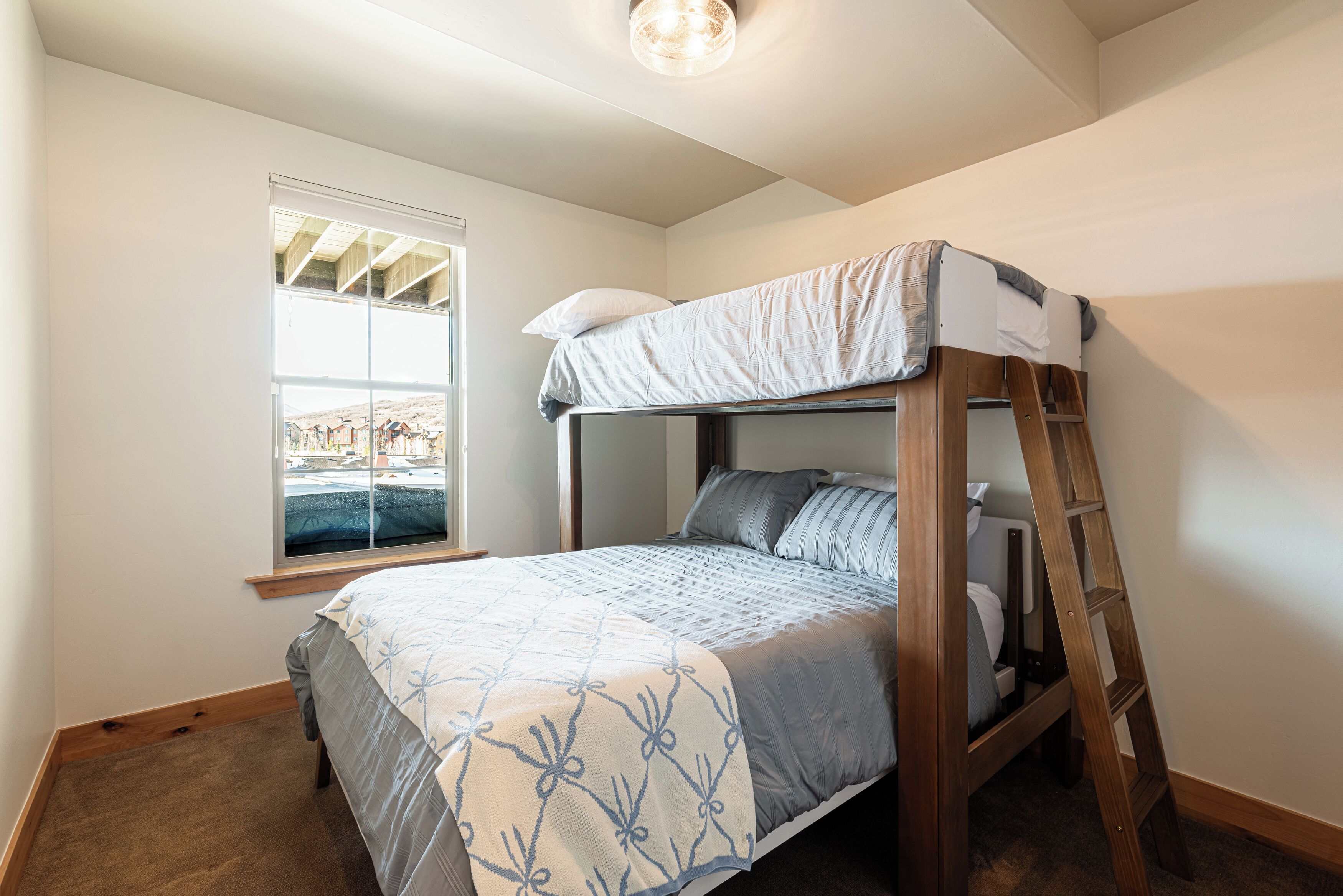 A bunk bed with a ladder, a window with blinds, and a carpeted floor.
