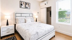 A bedroom with a bed, nightstands, a dresser, a closet, and a window with blinds. - Luxury New-Build Suite • Downtown • Convention (Hot Springs)