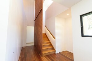 A modern interior with a wooden staircase, white walls, and a window. - Tree House by the Sea - Brand New Coastal Retreat with Ocean Views (Point Lookout)