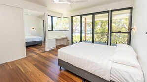 Ein modernes Schlafzimmer mit einem großen Bett, einem Schreibtisch und einem Balkon mit Blick auf Bäume.