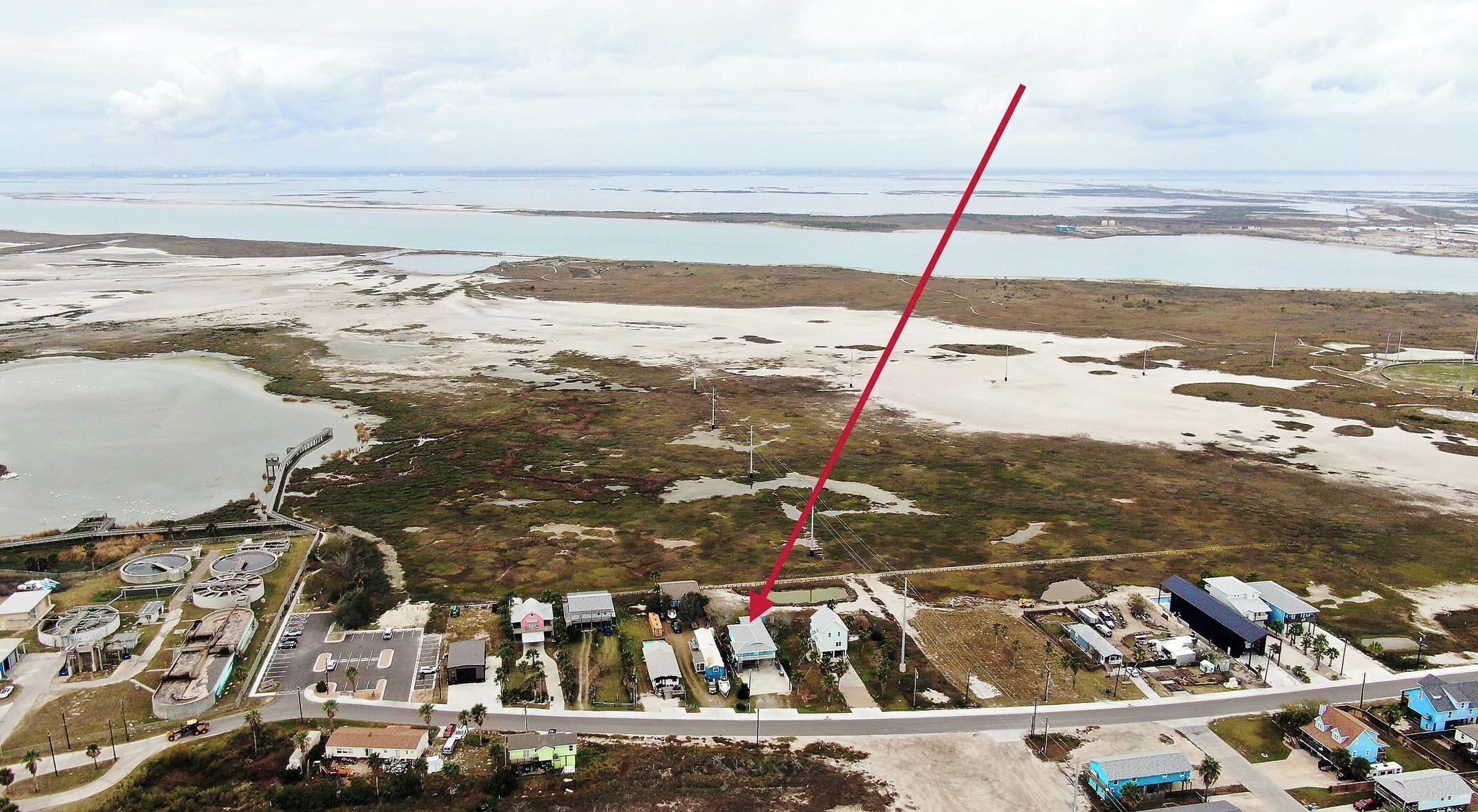 Luchtbeeld van een kustgebied met een brug, een jachthaven en een woonwijk met huizen en een parkeerplaats.