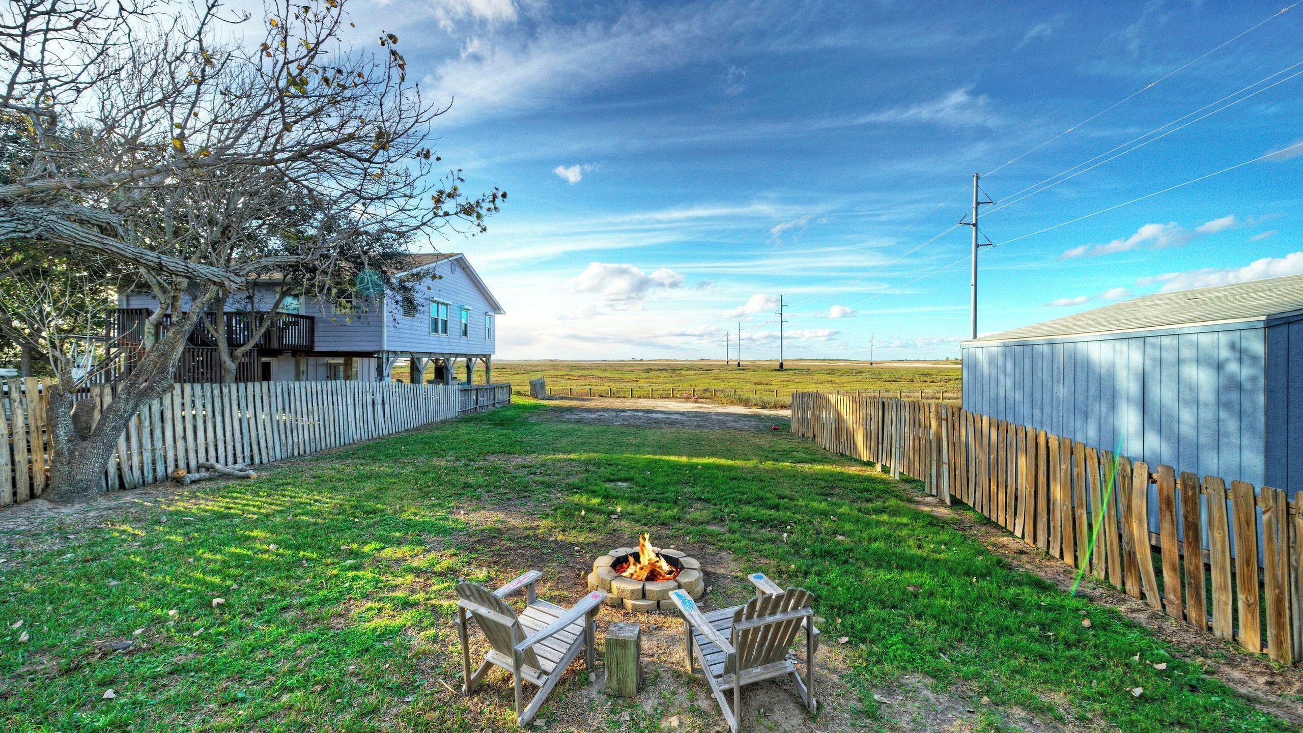 A house with a fire pit and chairs in the backyard.