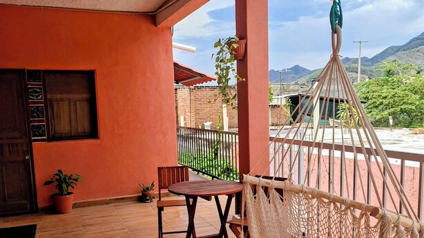 Ein Balkon mit Holzboden, einer Hängematte, einem Tisch und Stühlen mit Blick auf eine Berglandschaft.