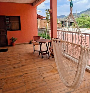 A wooden-floored balcony with a hammock, a table, and chairs, overlooking a mountainous landscape. - Rustic mexican charm mountain view 15 min beach, airport (Puerto Vallarta)