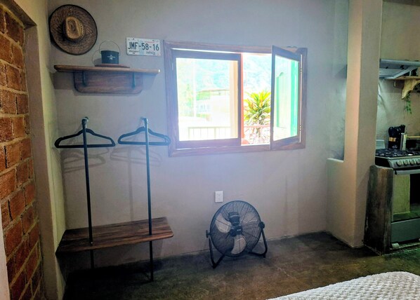 Una habitació amb finestra, ventilador, estufa i paret de maó.