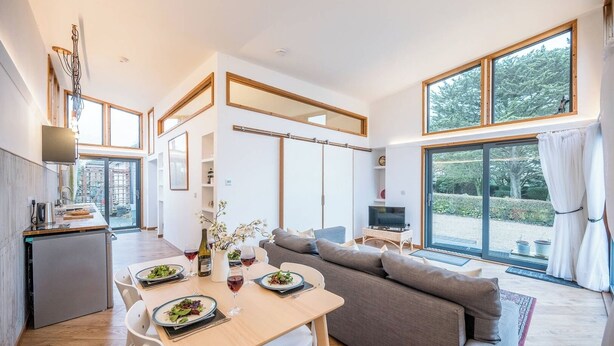 Ett modernt vardagsrum med matplats, soffa, TV och stora fönster som ger utsikt över omgivningen.