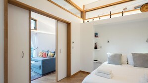 Ett modernt sovrum med en stor säng, ett sängbord, en garderob och utsikt över ett vardagsrum med en soffa och gardiner.