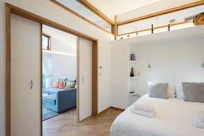 A modern bedroom with a large bed, a bedside table, a wardrobe, and a view of a living area with a sofa and curtains. - The Orchard Annexe, Framlingham (Framlingham)