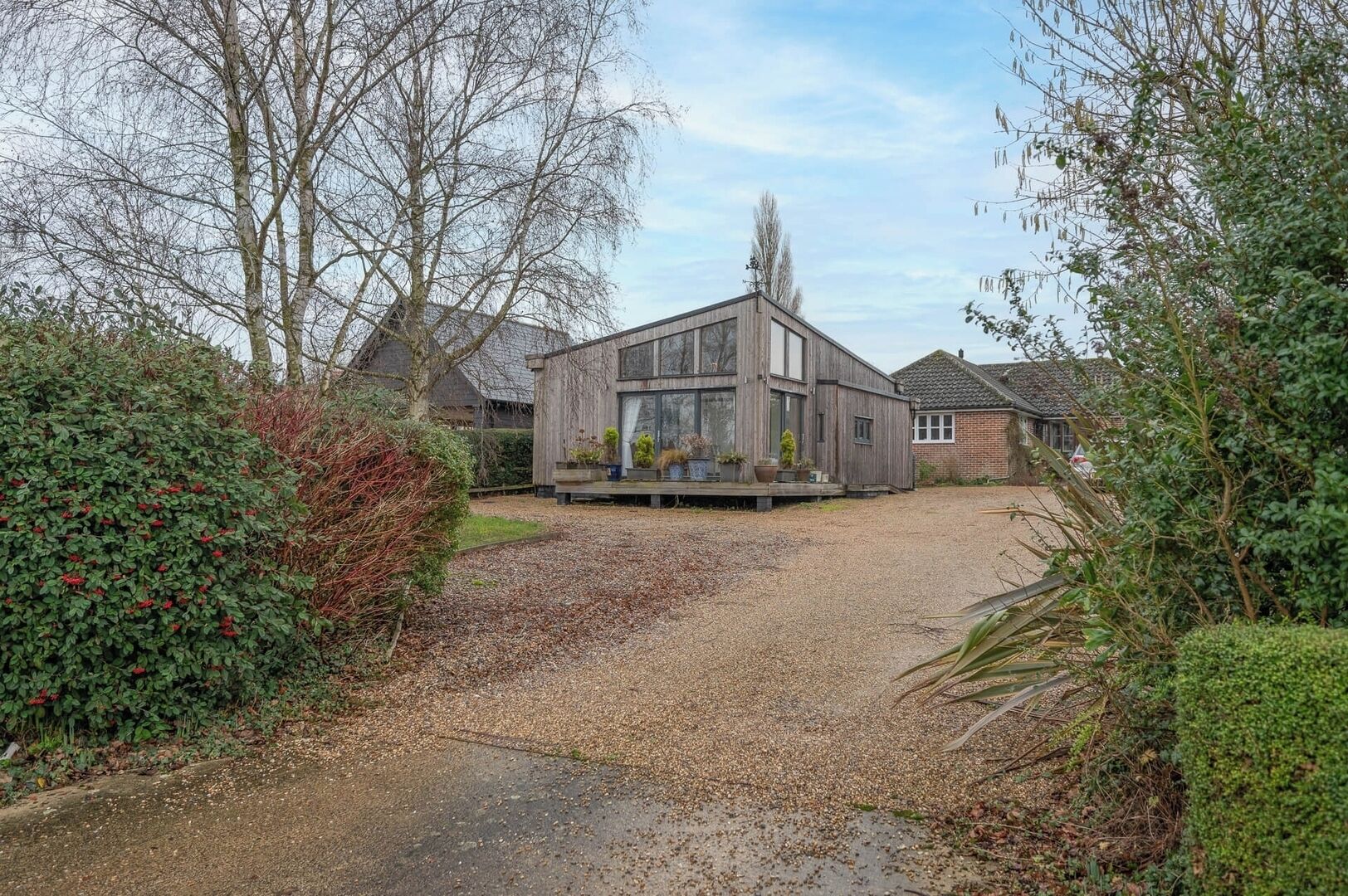 Une maison moderne avec une allée en gravier, entourée d’arbres matures et de haies bien entretenues.