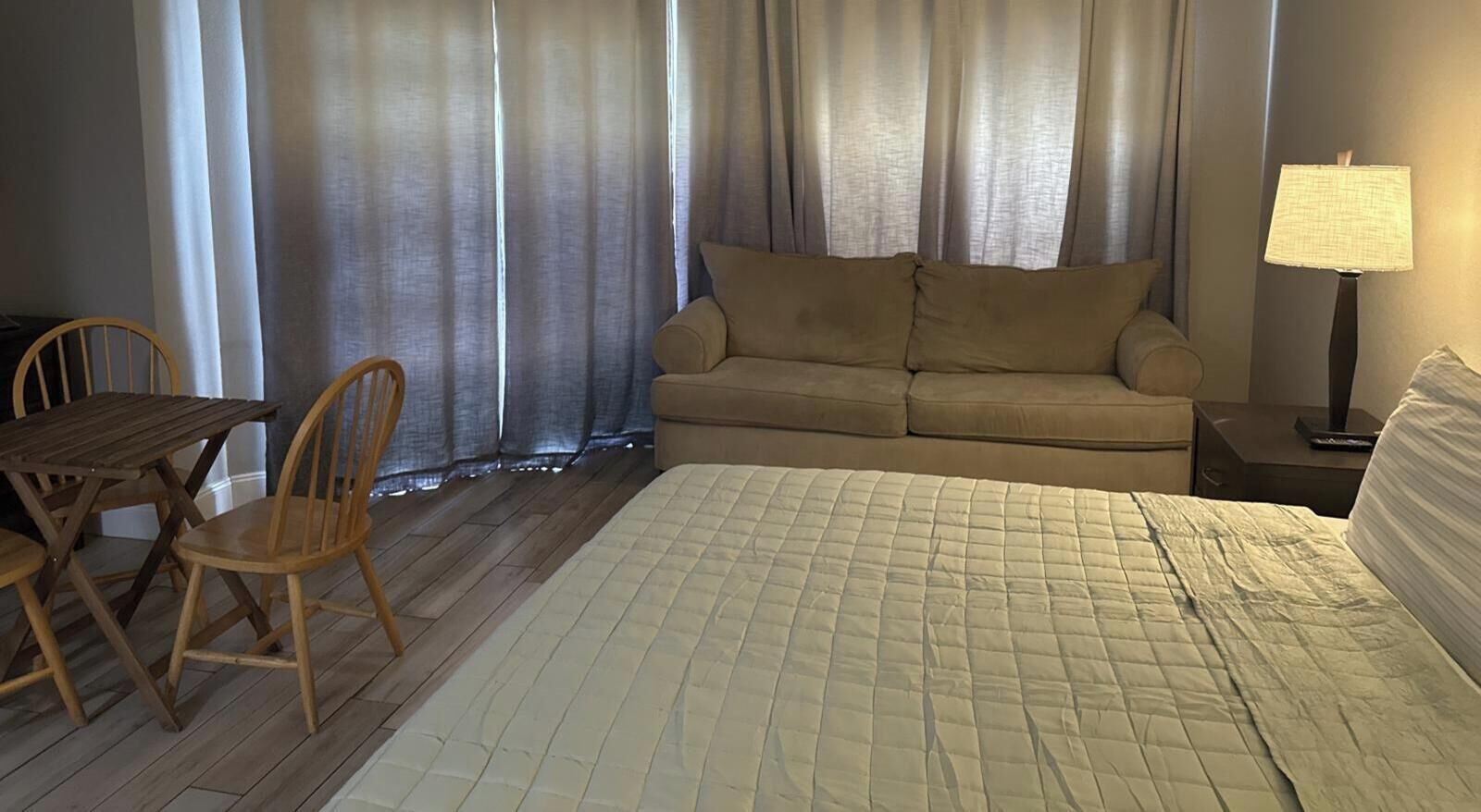 A hotel room with a bed, a sofa, a table with chairs, and a lamp.
