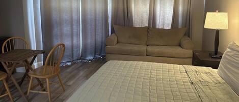 A hotel room with a bed, a sofa, a table with chairs, and a lamp.