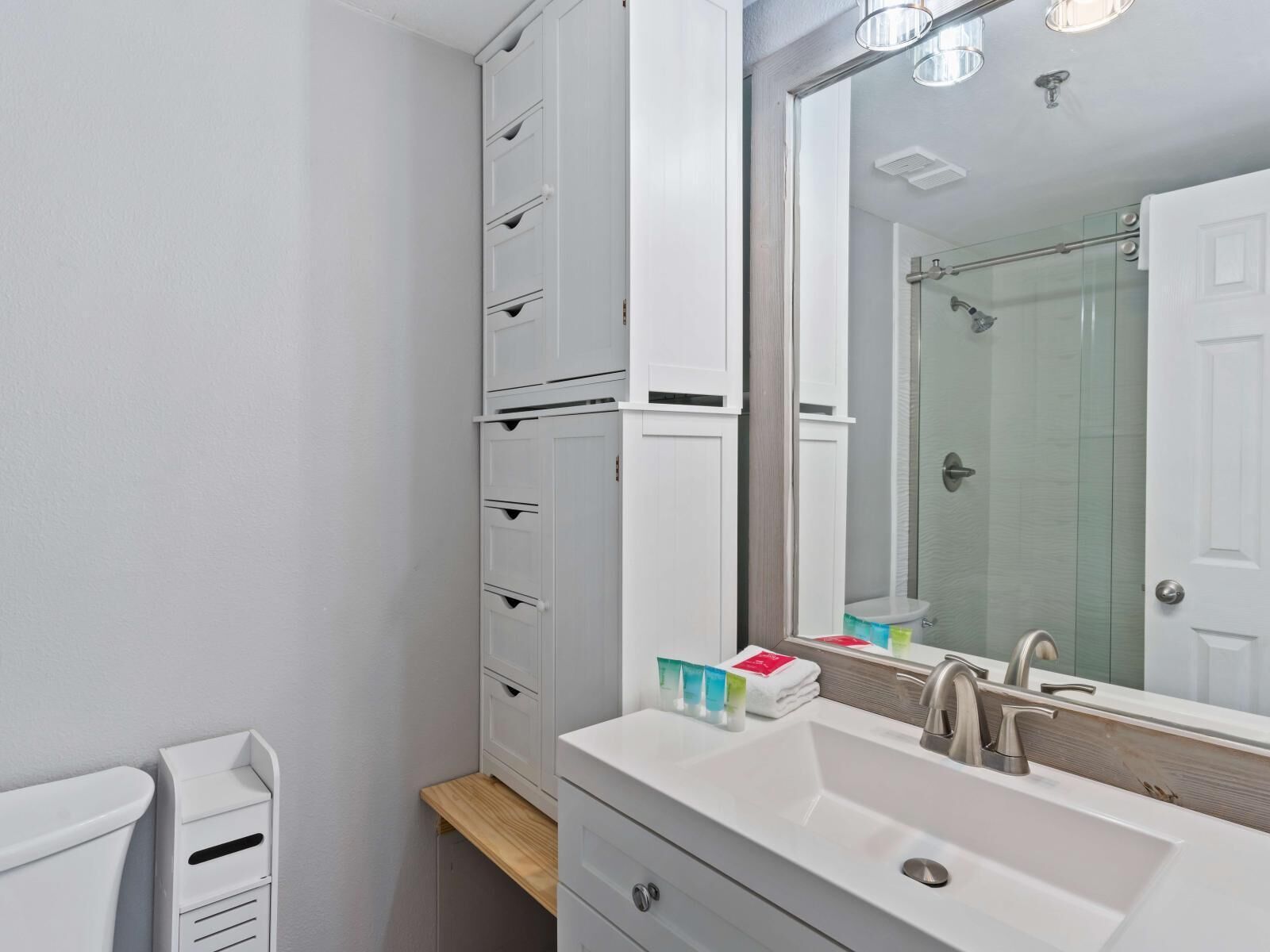 A modern bathroom with a white sink, mirror, and storage cabinets.