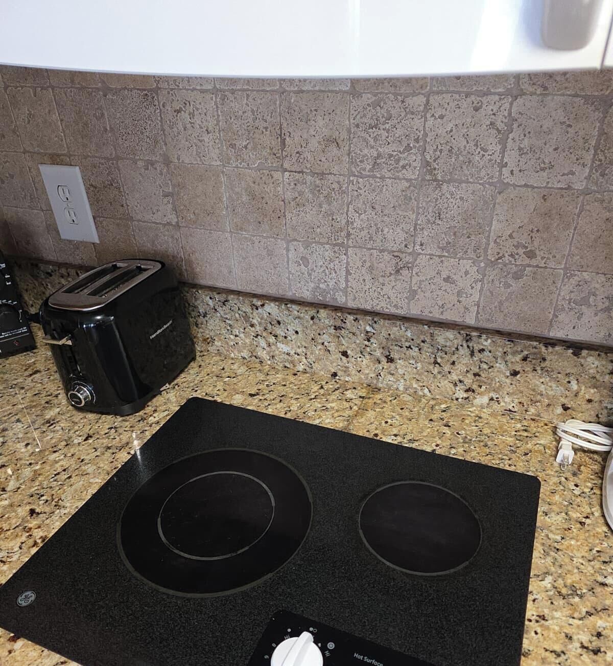 Una cocina con encimera de granito, un tostador negro y una cocina por inducción GE.