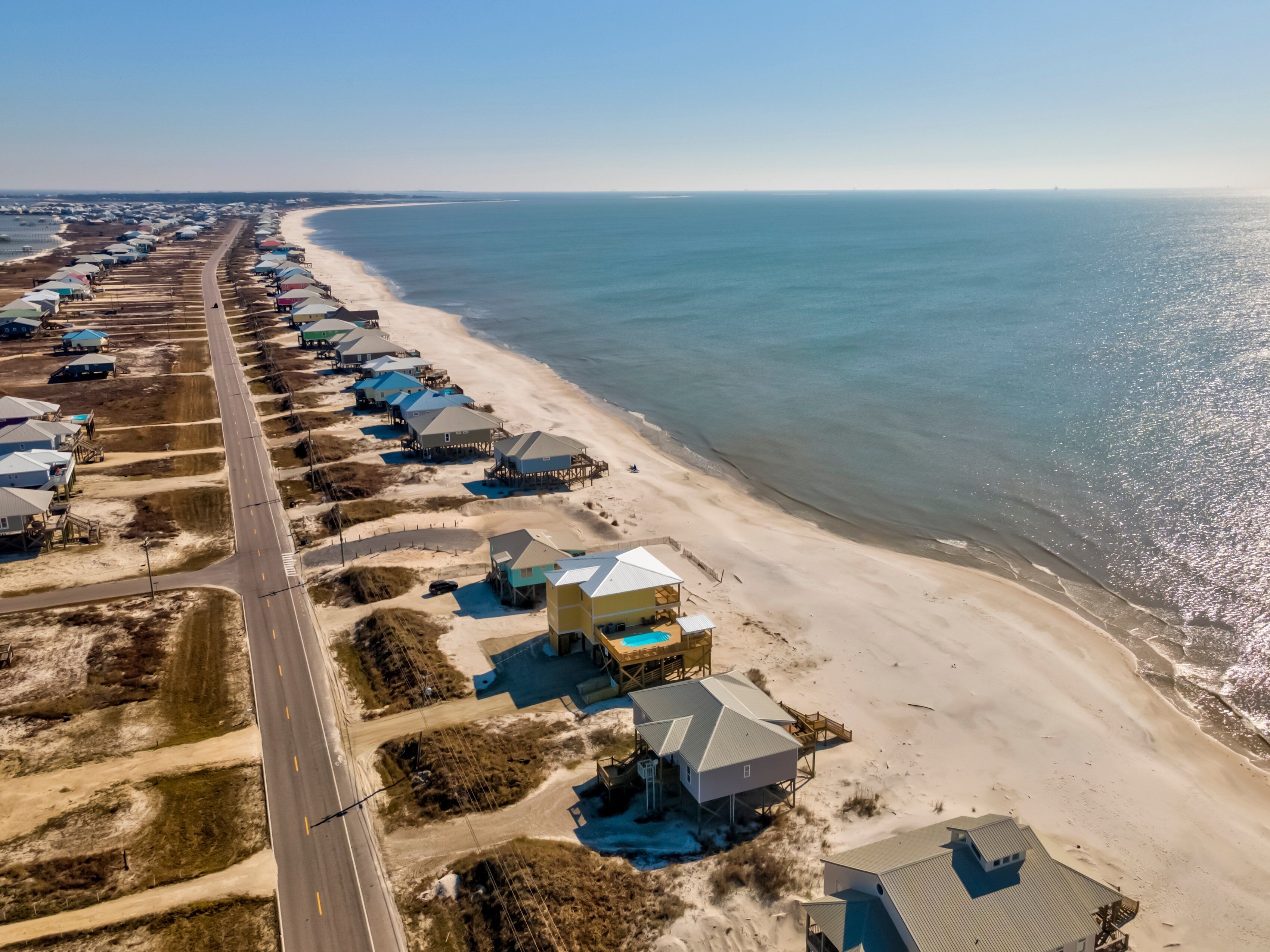 Vue aérienne d’une zone côtière avec des maisons de plage, une route et une plage.