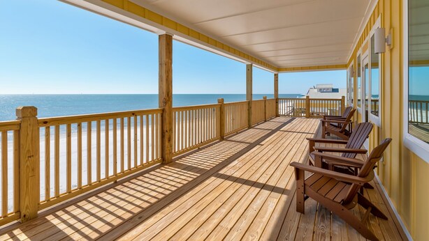 Un patio in legno con ringhiera, sedie di legno e vista sull'oceano.