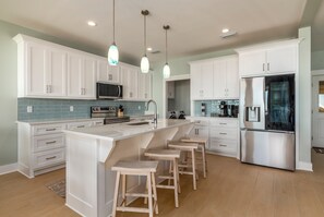 A modern kitchen with white cabinets, a stainless steel refrigerator, and a central island with bar stools. - NEW! Parrot Dice. On the beach, pool (Dauphin Island)