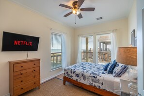 A bedroom with a bed, a wooden dresser, a ceiling fan, a TV mounted on the wall, and a balcony with a railing. - Ocean View l Pet Friendly (Gilchrist)