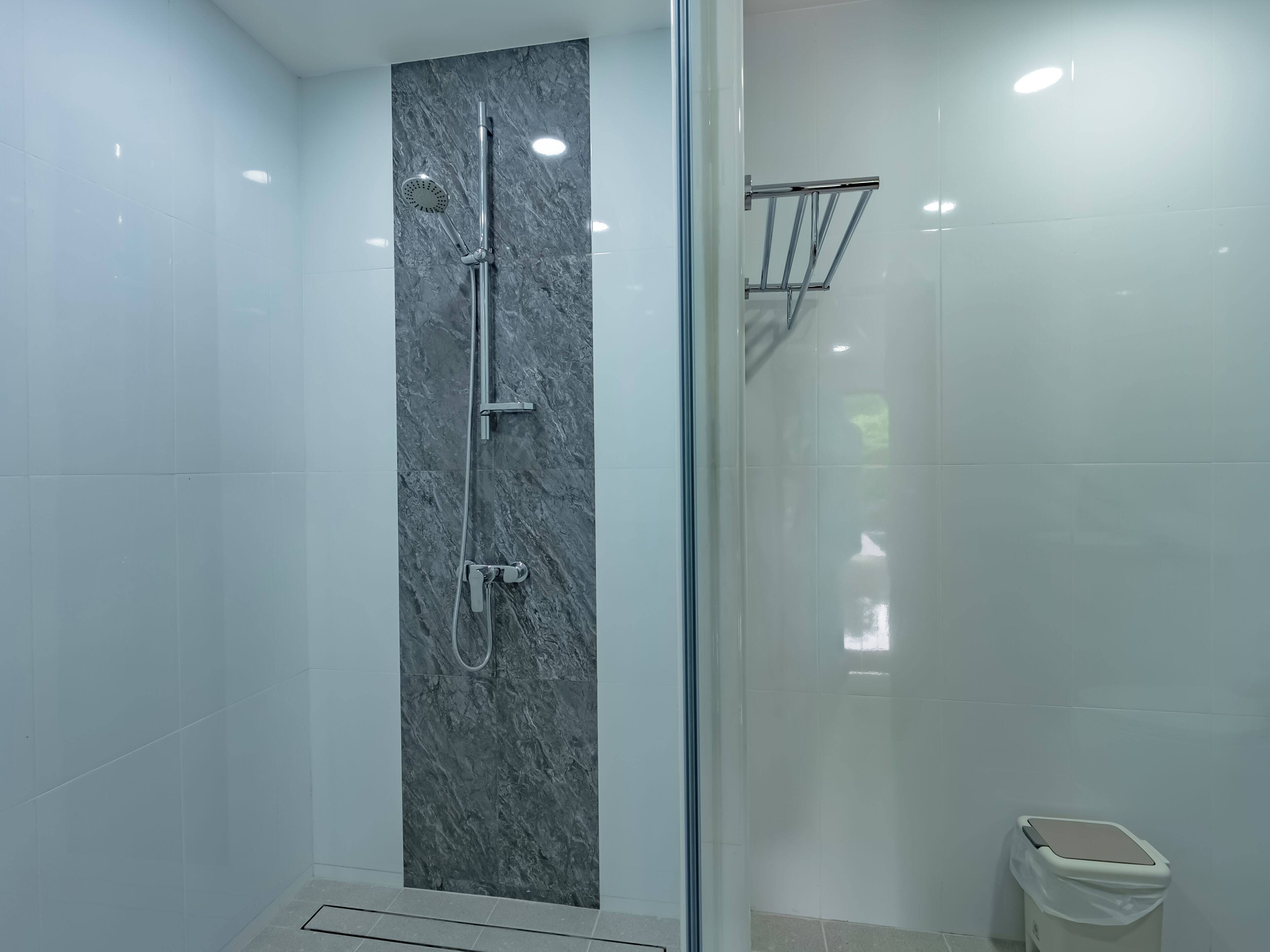 A modern bathroom with a glass-enclosed shower, a marble wall, and a white tiled floor.