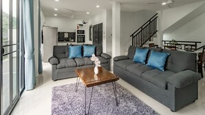 A modern living room with two grey sofas, a wooden coffee table, and a staircase leading to a dining area. - Valley View private pool Villa Phuket (Chalong)