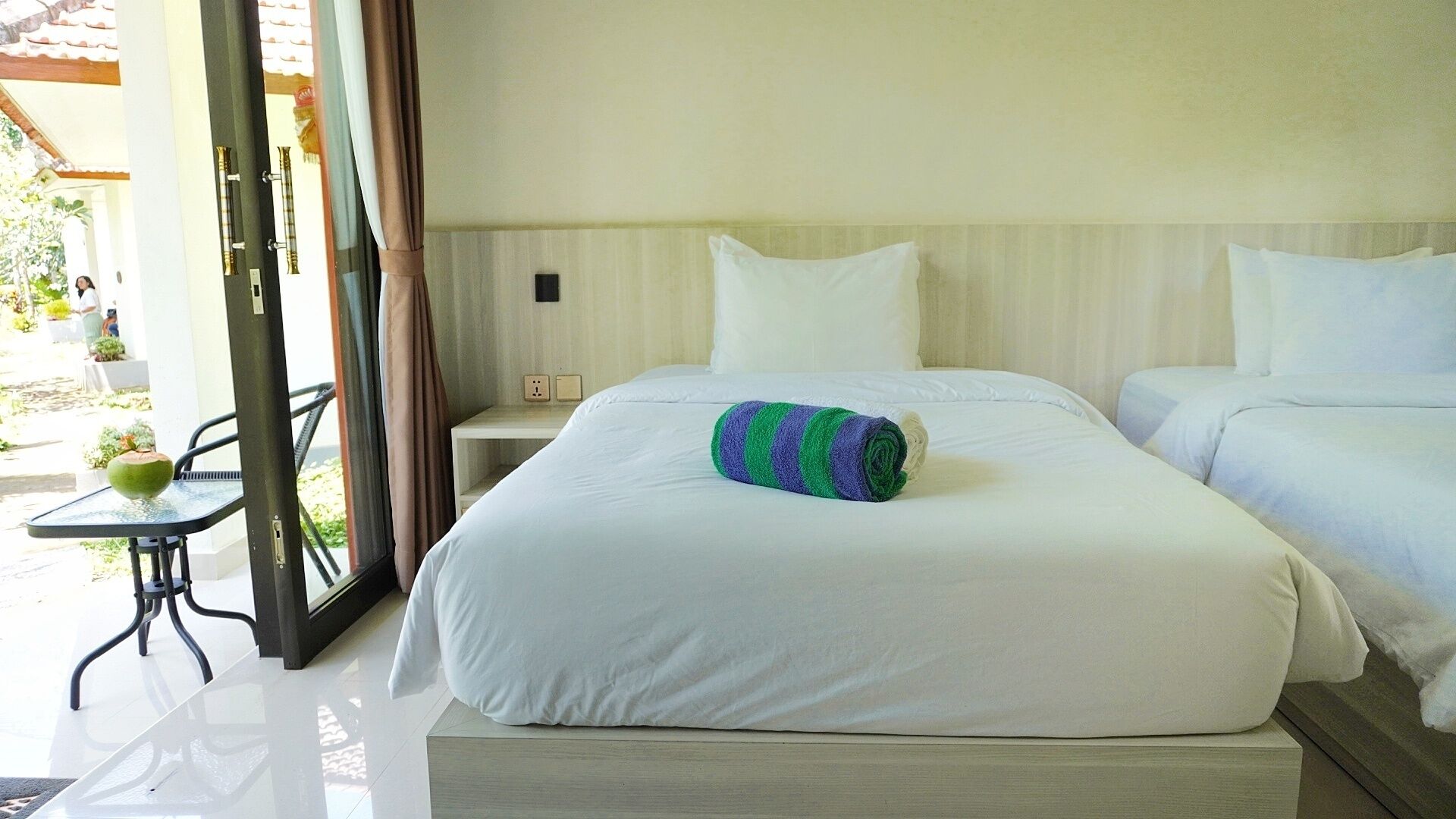Una habitación de hotel con dos camas, una mesita y vistas al exterior.