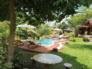 Un espace piscine agrémenté de chaises longues et de parasols, entouré d’une végétation luxuriante et doté d’une terrasse en bois.