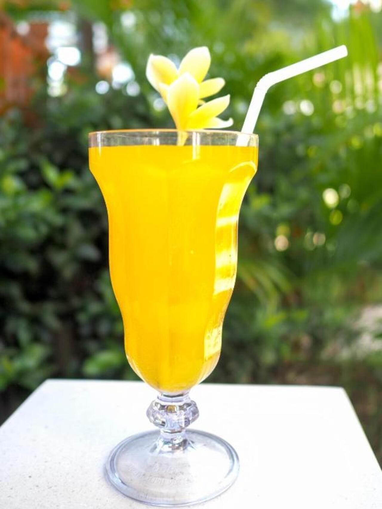 A glass of yellow drink with a straw and a flower garnish on a white surface.