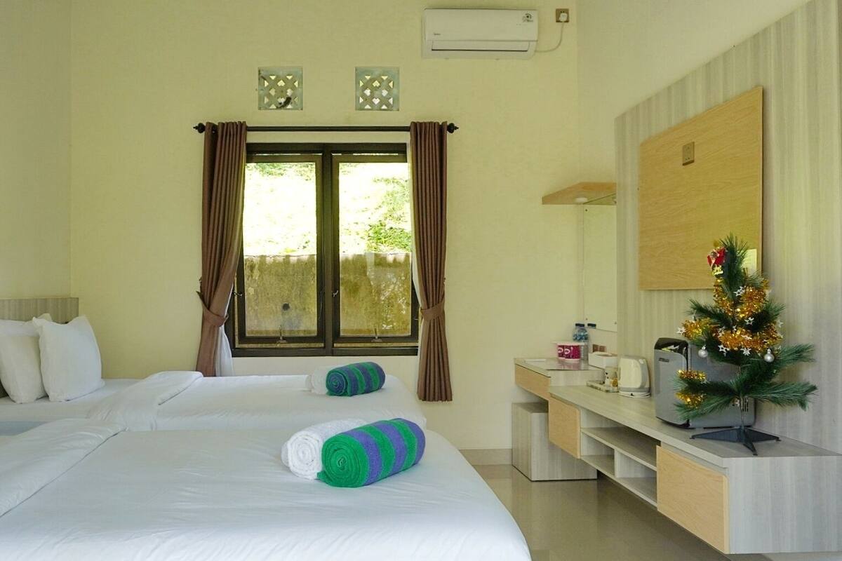 Habitación de hotel con cama, escritorio, silla, un pequeño árbol de Navidad y ventana con cortinas.