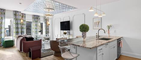 A modern kitchen with a central island, a dining area with a sofa and chairs, and a living room with a TV and decorative items.