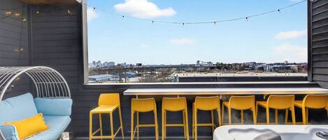 Un bar sur le toit offrant une vue sur la ville, avec des fauteuils suspendus, des chaises jaunes et un jacuzzi.