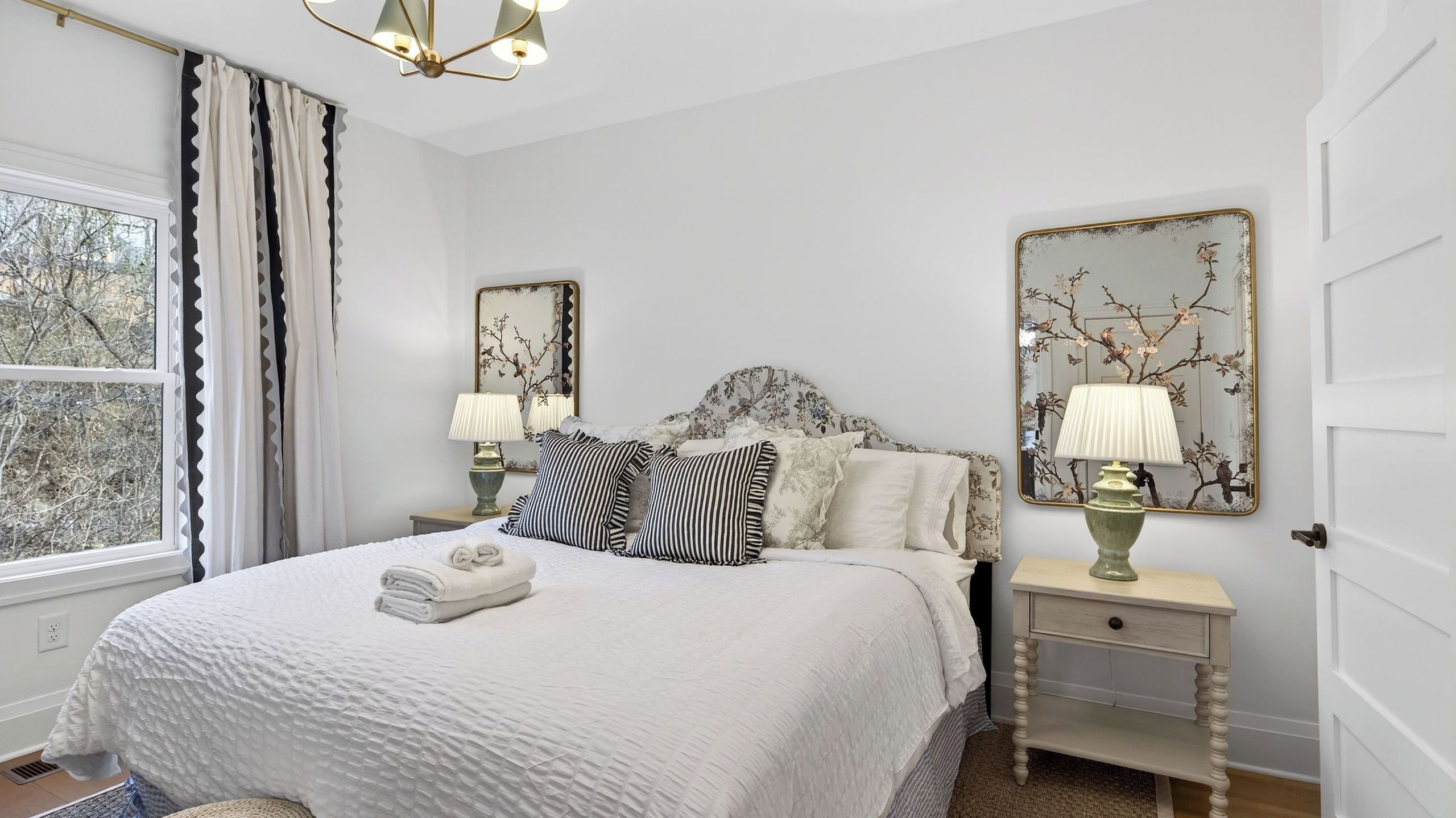 A neatly arranged bedroom with a large bed, two bedside tables with lamps, and two wall-mounted mirrors.