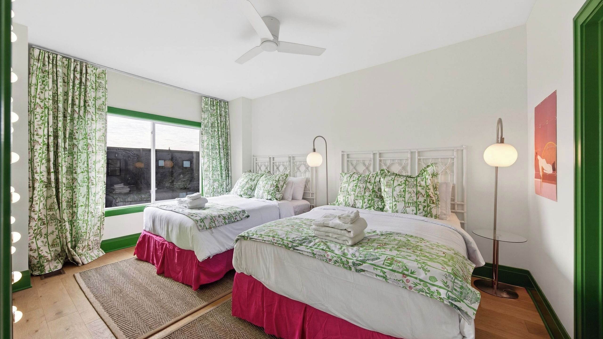 A bedroom with two beds, a ceiling fan, a floor lamp, and a view of the outside.