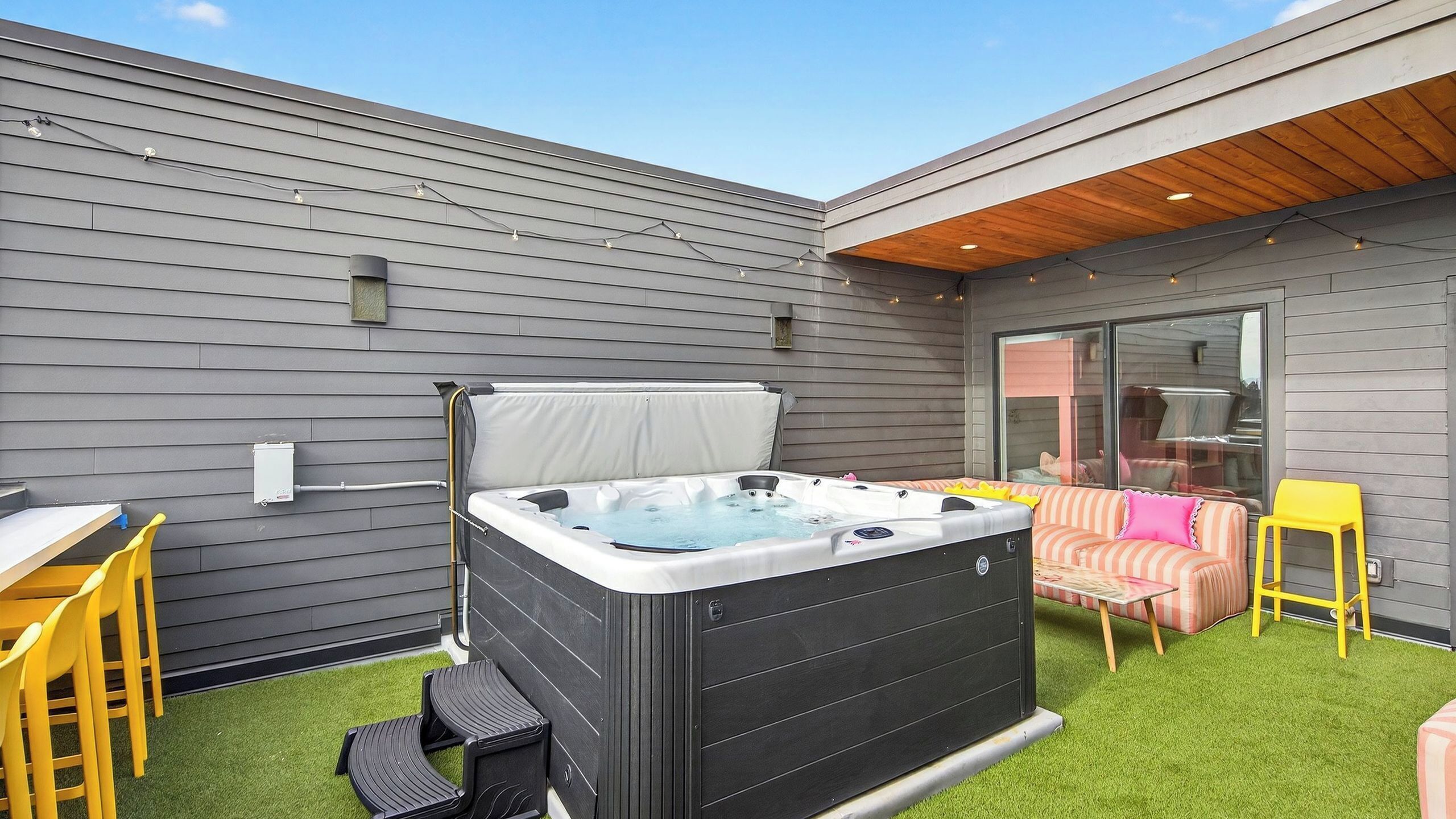 A backyard with a hot tub, a table, chairs, and a sofa.