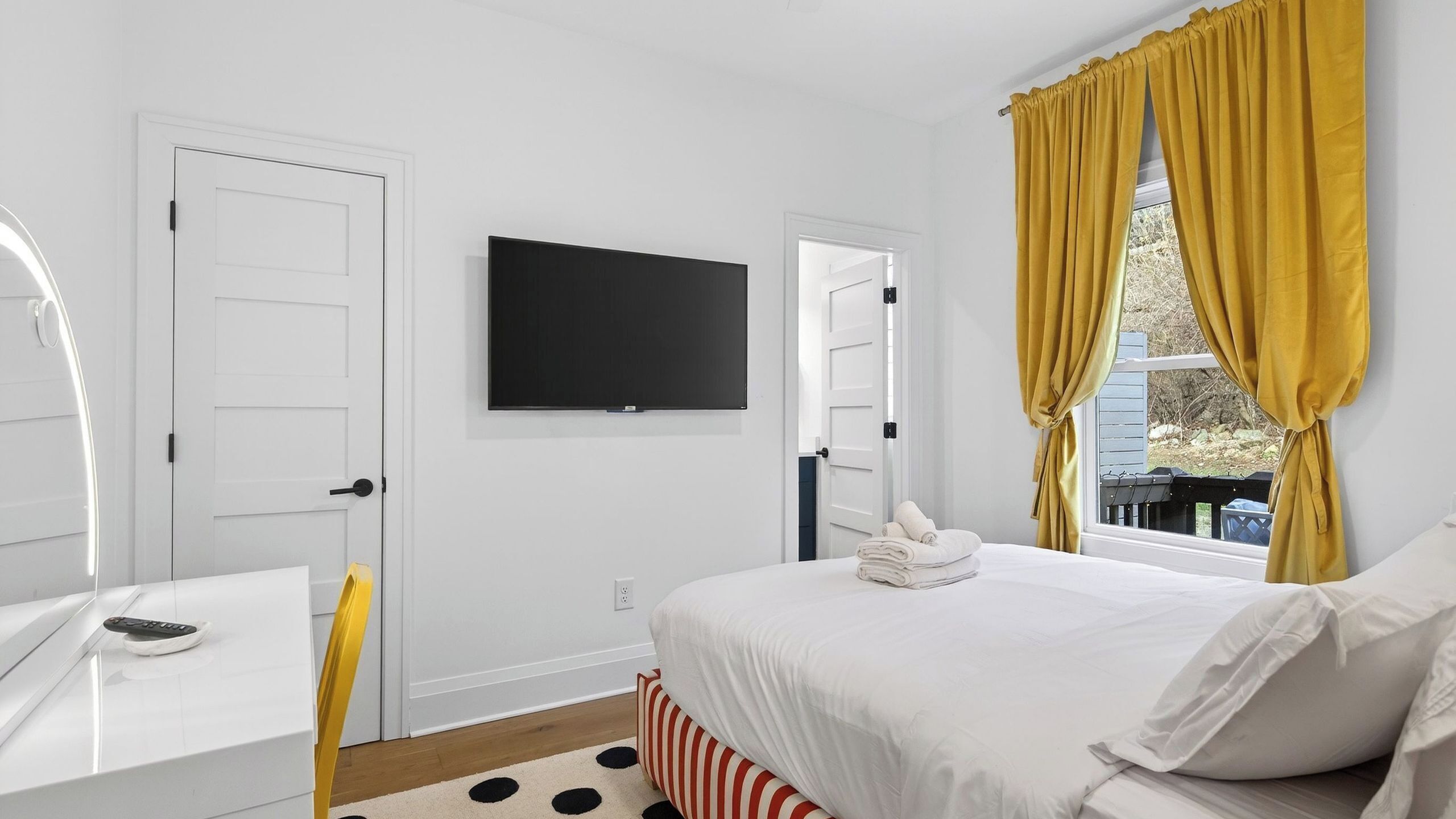 A bedroom with a bed, a TV, a desk, and a window with curtains.