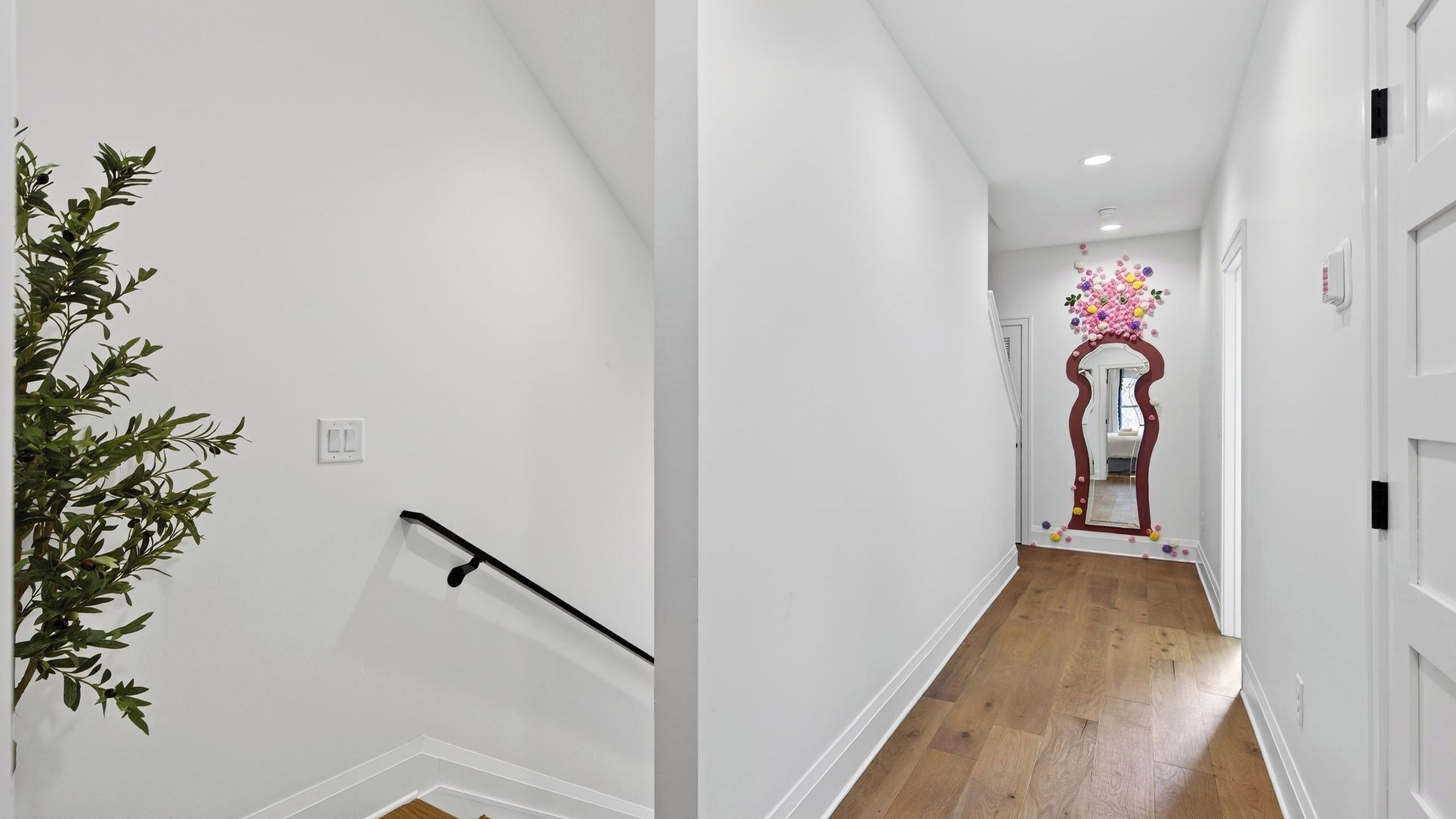 Un couloir aux murs blancs, doté d’un plancher en bois, d’une rambarde noire et d’un miroir décoratif orné de motifs floraux.