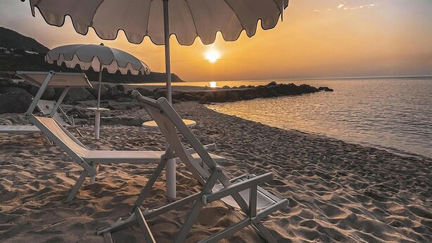 Een strandscène met een zonsondergang, met een rij lege strandstoelen en parasols.
