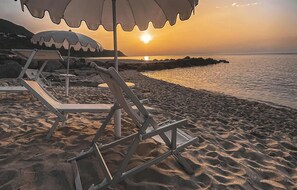 Une scène de plage au coucher du soleil, avec une rangée de chaises de plage et de parasols vides.