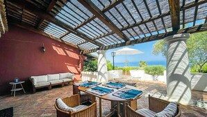 Een terras buiten met een tafel, stoelen, een bank en uitzicht op de oceaan.