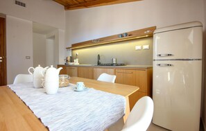 A modern kitchen with wooden cabinets, a white refrigerator, and a dining table set with white chairs and a striped tablecloth. - Awesome apartment in San Marco di Castellab (San Marco di Castellab)