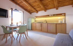 Une cuisine compacte avec des meubles en bois, un four encastré et un évier. On y trouve un coin repas avec une table et des chaises, ainsi qu’un canapé dans l’espace salon.