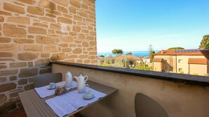 A balcony with a stone wall, a table with a teapot, cups, and a jar of cookies, overlooking a coastal town with houses and the sea. - Gorgeous apartment in San Marco di Castellab (San Marco di Castellab)
