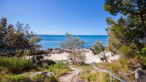 A coastal path leading to a beach with clear blue water and rocky outcrops.