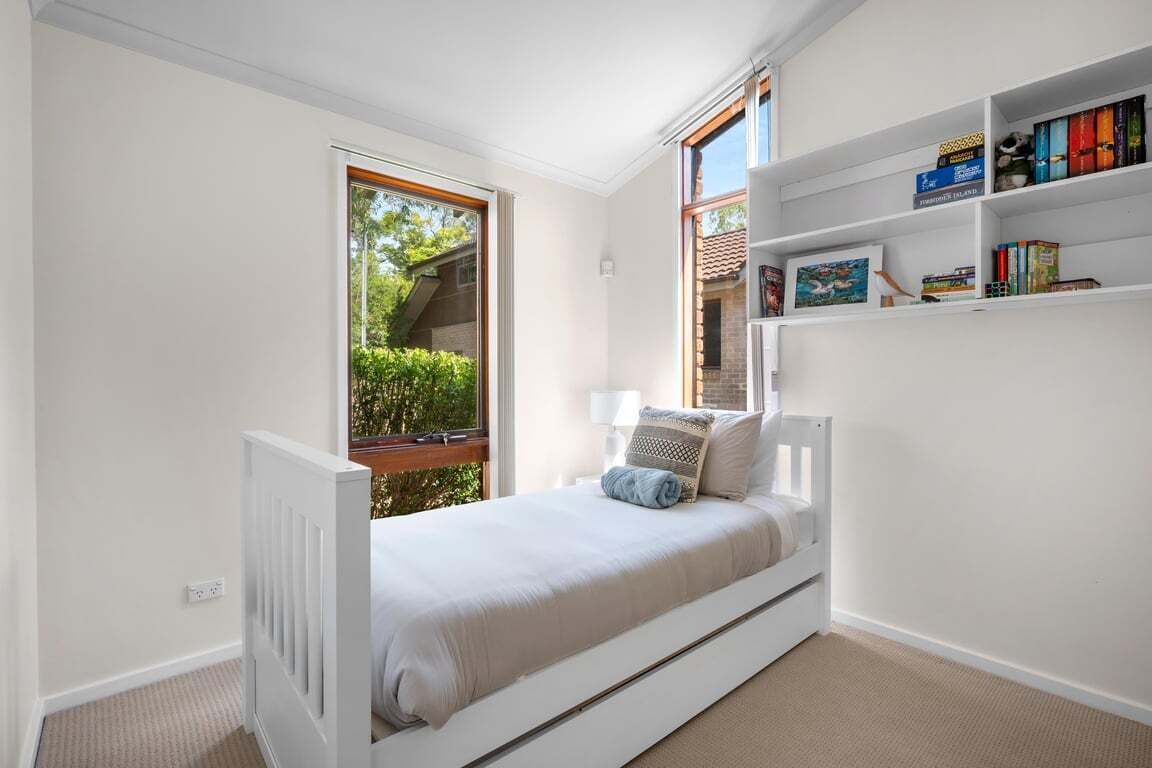 Une chambre à coucher avec un lit blanc, une fenêtre et une bibliothèque.